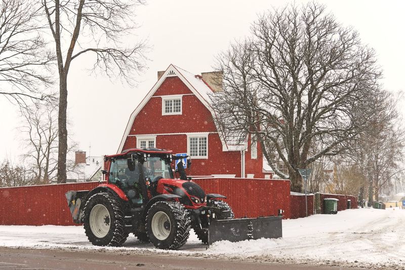 Rød traktor med brøyteskjær foran en rød låve