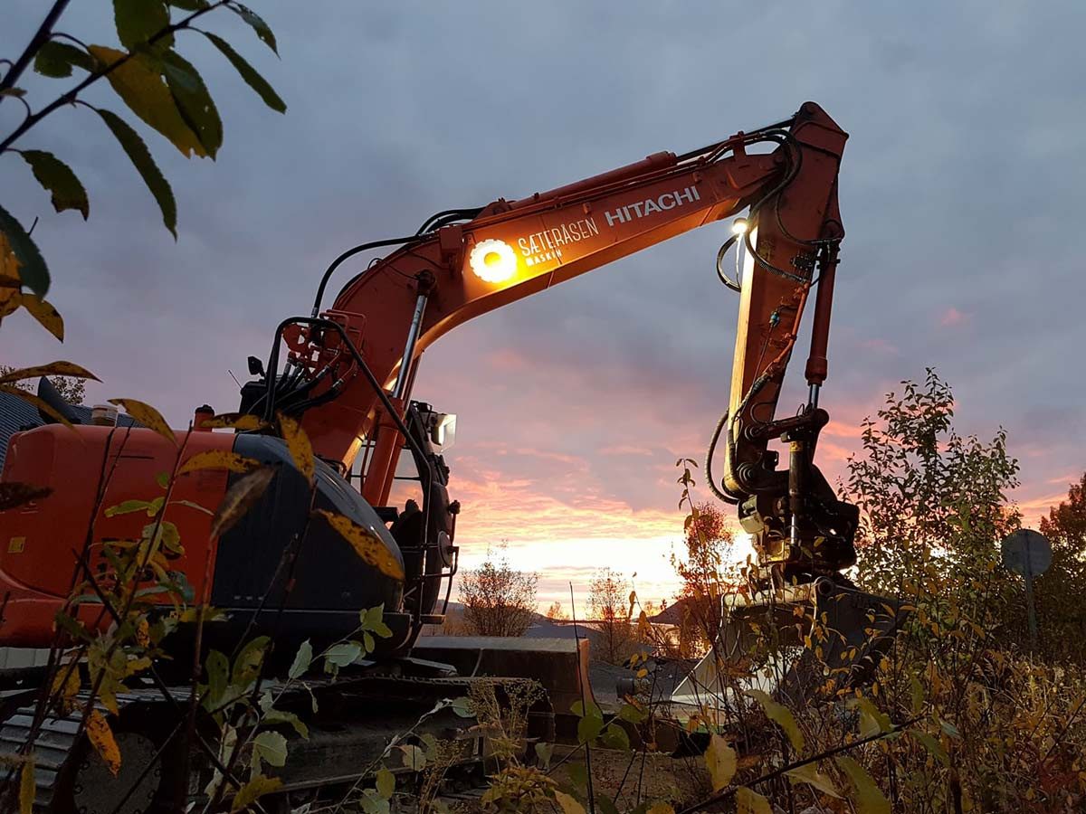 Sæteråsens Hitachi-gravemaskin med logo på bommen, i solnedgang